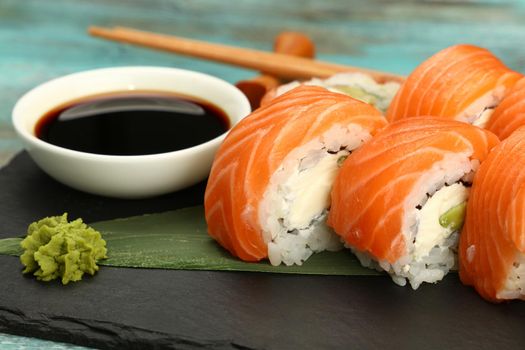 Close up set of six Philadelphia sushi rolls with raw salmon served on black slate board on blue table, high angle view