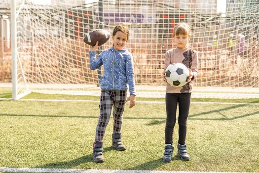 Little football team: toddler girls with soccer ball at football field