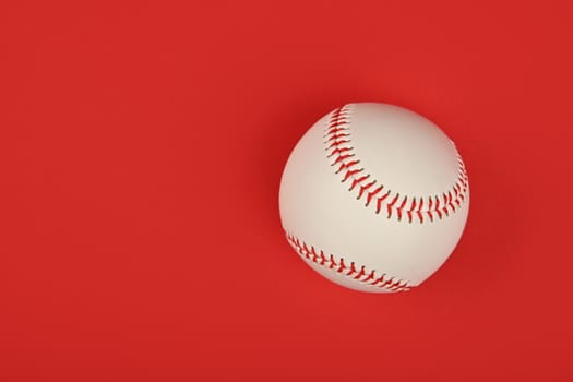 Close up one new baseball ball with red stitch over vivid red background, elevated top view, directly above