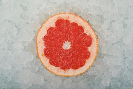 Close up one fresh juicy pink grapefruit slice over background of crushed ice, elevated high angle view, directly above