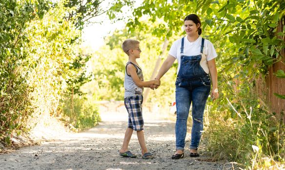 Pregnant woman walking countryside with her son. Child hugging his pregnant mother.