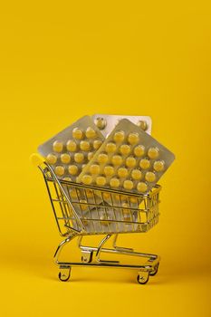 Close up several different blister packs of pills in small shopping cart over yellow background, concept of online medicine order delivery, low angle view