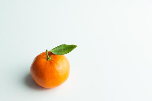 tangerine with green leaf in bottom left on white background with soft light