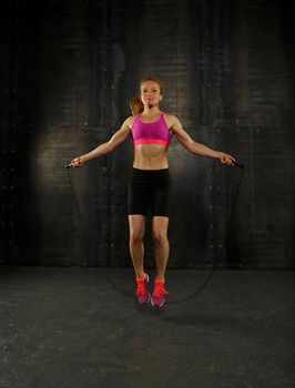 One young middle age athletic, woman training, exercising with fitness jumping rope over dark background, full length front view, looking at camera