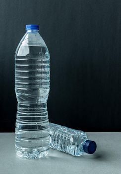 two plastic bottles filled with mineral water one large standing and one small lying with blue caps and black background
