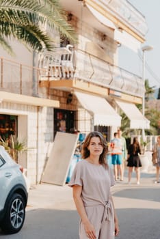 Girl tourist walking through ancient narrow street on a beautiful summer day in MEDITERRANEAN MEDIEVAL CITY , OLD TOWN bUDVA, MONTENEGRO. Young beautiful cheerful woman walking on old street at tropical town. Pretty girl looking at you and smiling