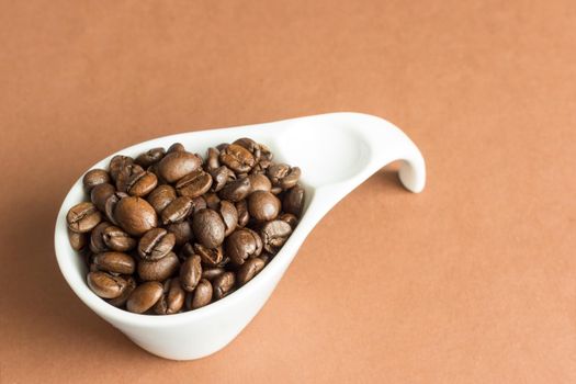 White oval ceramic bowl filled with coffee beans on light brown background