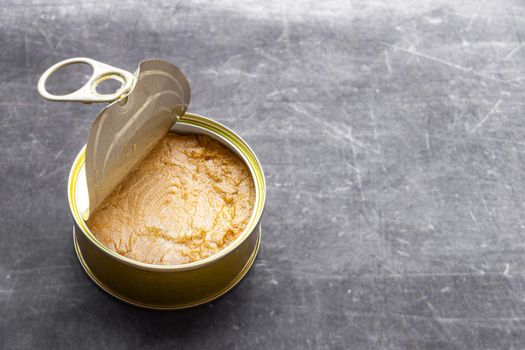 close up of a half open light tuna canning tin with hard natural light and gray background