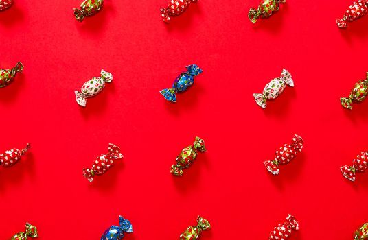 Christmas chocolates placed forming a pattern on a red background alternating chocolates with red green blue and white wrapper