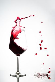 vertical backlit image of a glass of red wine with splashes at high speed through the air splashing the glass surface on which the glass rests