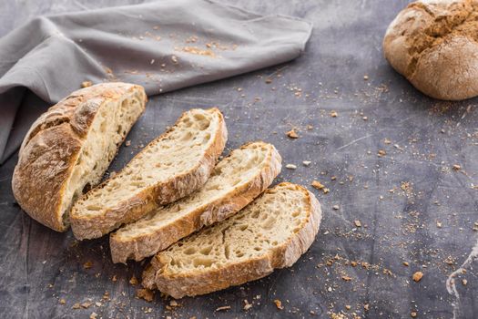 image at forty-five degrees of an organic bread divided into slices placed in a fan shape on a dark surface surrounded by crumbs and a gray cloth with natural light