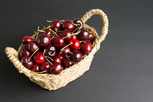 wicker basket full of cherries on black background in landscape with negative space to the right of the image