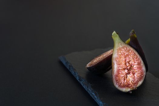 fresh sliced figs placed vertically on black slate table on black background horizontally with natural light