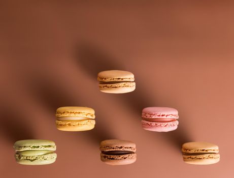 horizontal image of six macorons of various colors placed in the shape of a triangle at the bottom of the image on a chocolate brown background with soft lighting