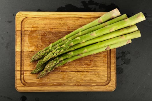 Close up bunch of washed fresh green asparagus on wooden cutting board with drops of water, elevated top view, directly above