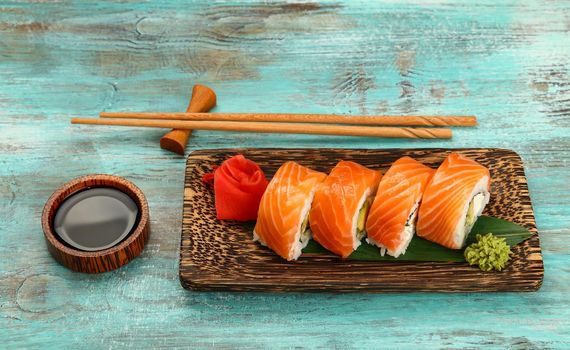 Close up one set of six Philadelphia sushi rolls with raw salmon served on palm wood plate on blue table, higgh angle view