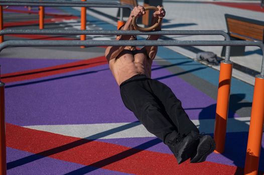 Shirtless man doing horizontal balance on parallel bars at sports ground