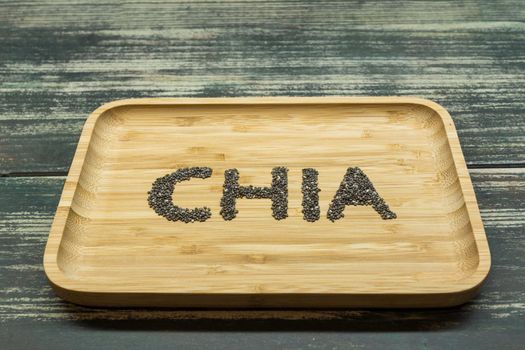 takes in perspective the word chia written with the seeds of the chia itself on a bamboo tray on top of some wooden boards aged in dark tones