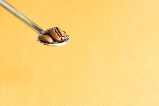 Teaspoon with three coffee beans on yellow background