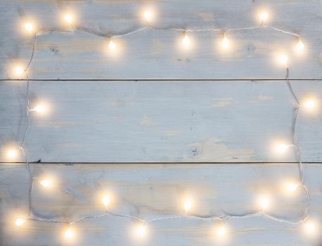 garland of round christmas lights with warm color placed in the form of a frame on light background of wooden planks