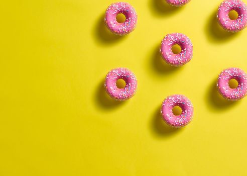 pattern of pink donuts decorated with colored confetti with shadow on lemon yellow background