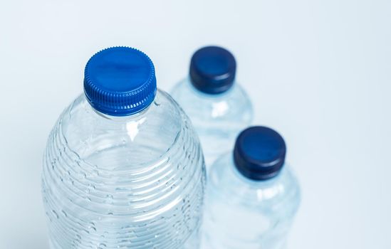 three empty plastic bottles with blue caps seen from above one in the foreground in focus and two other smaller ones behind out of focus on white background