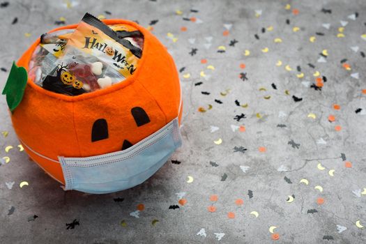 halloween pumpkin made of fabric with mask filled with jelly beans on background decorated with halloween motifs