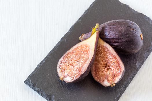 fresh cut figs on a black slate board on white background horizontally scratched in natural light