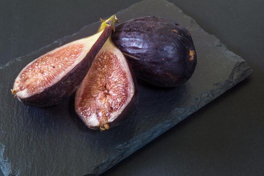 fresh cut figs on a black slate board on a black background horizontally in natural light