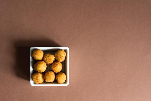 Croquettes in white ceramic ceramic bowl viewed from above on light brown background