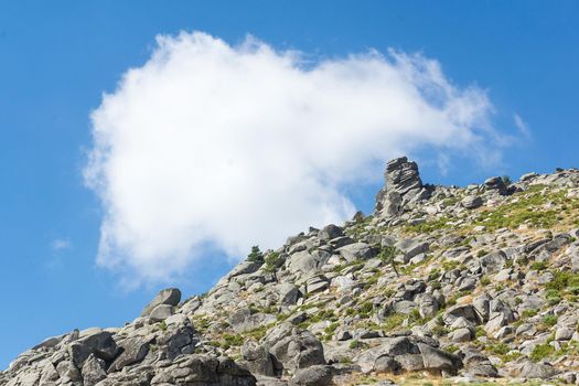 horizontal image of a rocky mountain slope forming a diagonal with the blue sky with a white cloud in the background