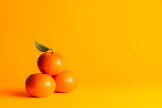 three tangerines stacked in the lower left corner in a triangle shape with an orange background and side lighting