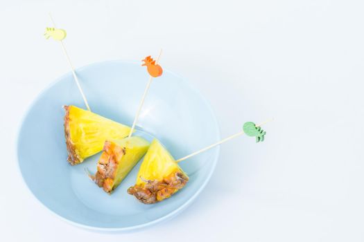 Pineapple skewers peeled and cut into triangles with chopsticks decorated inside a blue bowl with white background