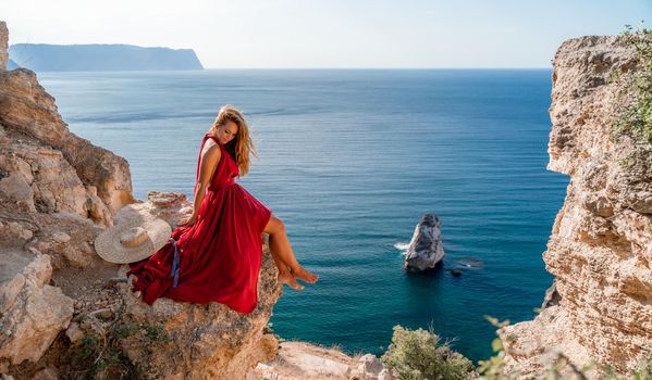 A girl with flowing hair in a long red dress sits on a rock above the sea. The stone can be seen in the sea