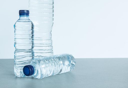 three plastic bottles filled with mineral water two standing and one lying down with blue caps on white background