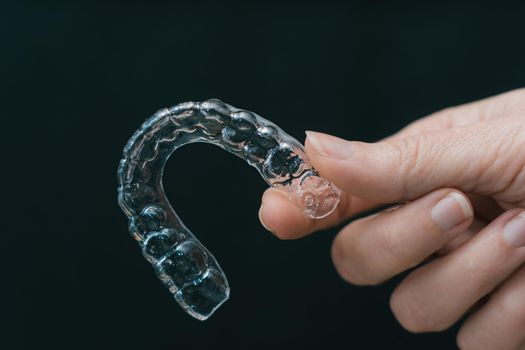 closeup of woman's hand holding a side lit transparent retainer on black background