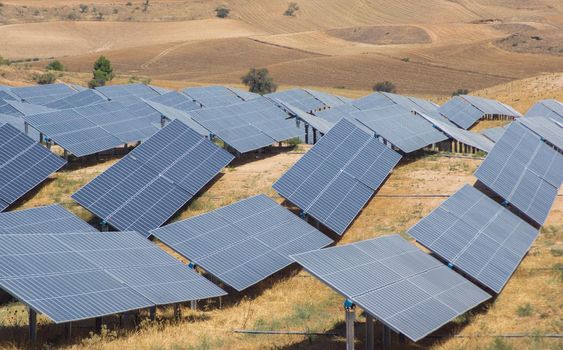 image of solar panels on a summer day forming waves that adapt to the terrain as if they were sea waves with a background of brown crop fields in the background