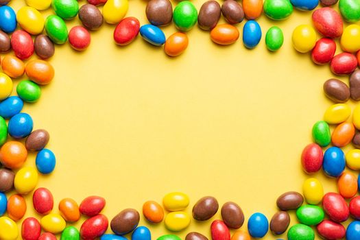 colored crunchy chocolate balls placed around the image leaving copy space on a yellow background