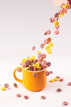 colored cereal rings falling into an orange cup on white background with side lighting