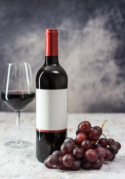 image of red wine bottle with bunch of grapes and wine glass on gray toned background with side natural light