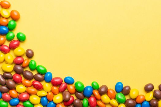 colored crunchy chocolate balls placed in the lower left corner on a yellow background