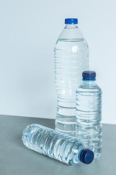 three plastic bottles filled with mineral water two standing and one lying down with blue caps on white background