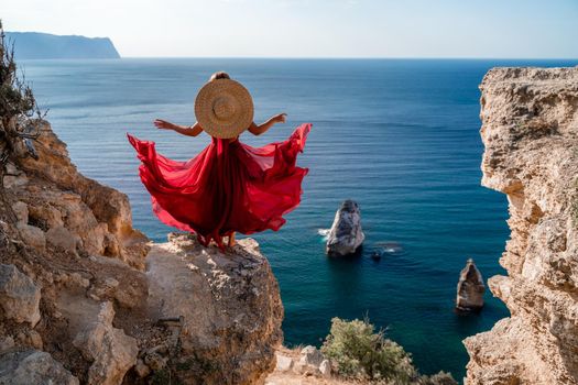 A woman in a flying red dress fluttering in the wind and a straw hat against the backdrop of the sea