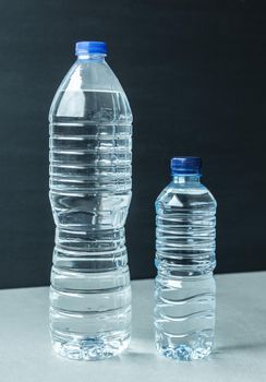 two plastic bottles filled with mineral water one large and one small with blue caps and black background