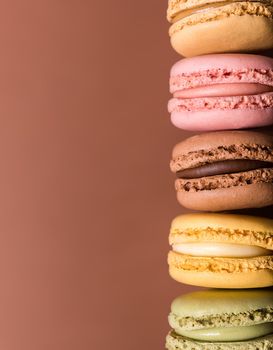 vertical image of five macarons aligned to the right vertically in macro close-up on chocolate brown background with soft side lighting