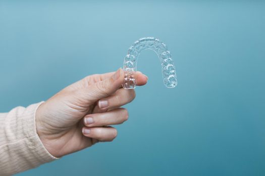 woman's hand holding a side lit transparent retainer on blue background