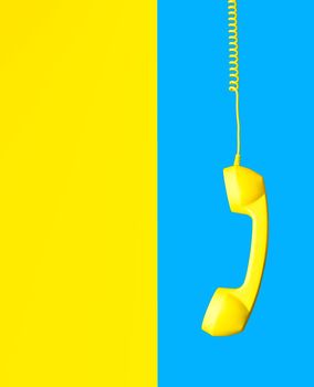 yellow retro phone hanging on spiral cord on background split in half in sky blue and yellow