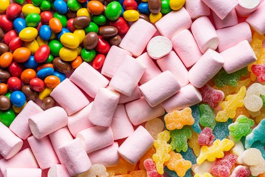 close-up of colored animal jelly beans colored chocolate balls and pink marshmallows placed in three diagonal lines occupying the entire image