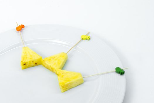 Pineapple skewers peeled and cut into triangles with chopsticks decorated on white plate on white background