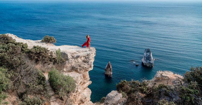 A woman in a red flying dress fluttering in the wind, against the backdrop of the sea